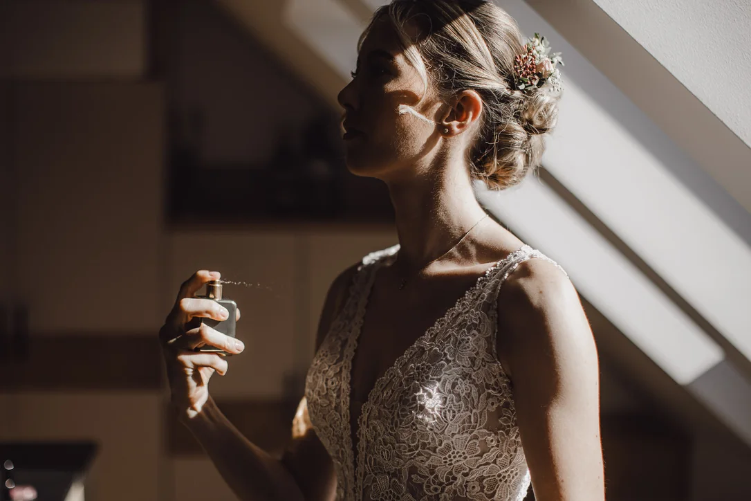 Braut sprüht sich im starken Fensterlicht beim Getting Ready Parfum auf