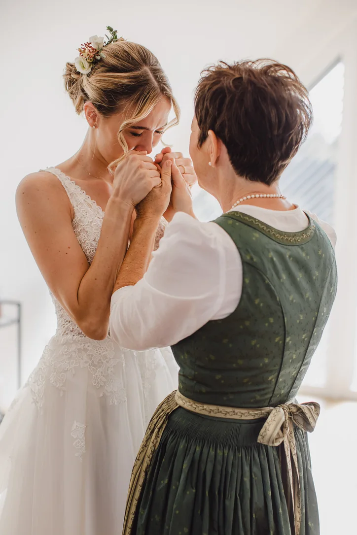 Braut teilt beim Getting Ready einen emotionalen Moment mit einer Frau im grünen Dirndl