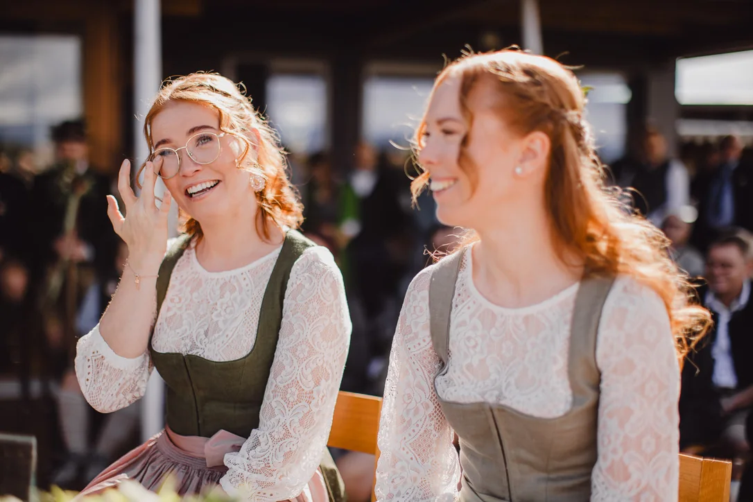 Zwei Hochzeitsgäste in Dirndl lachen und wischen sich während der Trauung gerührt die Augen