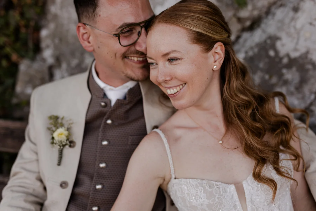 Lachendes Brautpaar bei der Trachtenhochzeit vor einer alten Steinmauer in Traunkirchen
