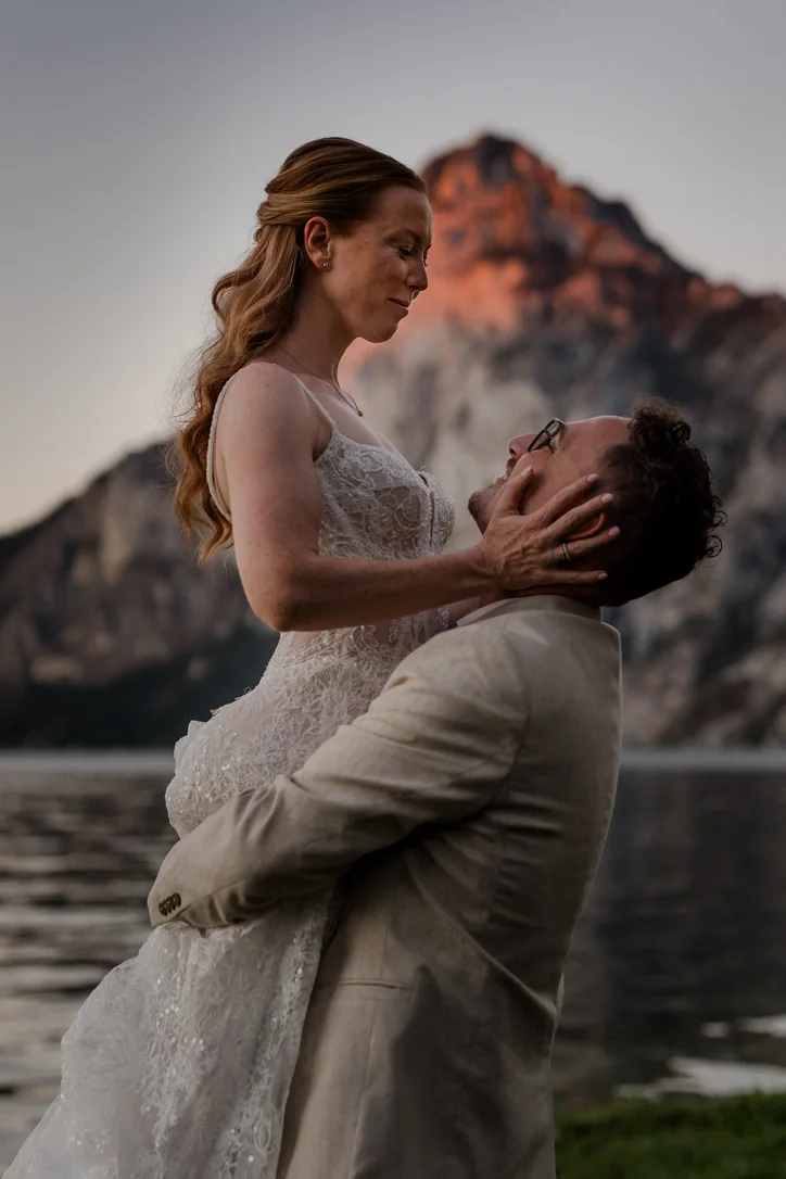 Bräutigam hebt die Braut vor dem Traunsee und den Bergen bei Sonnenuntergang hoch