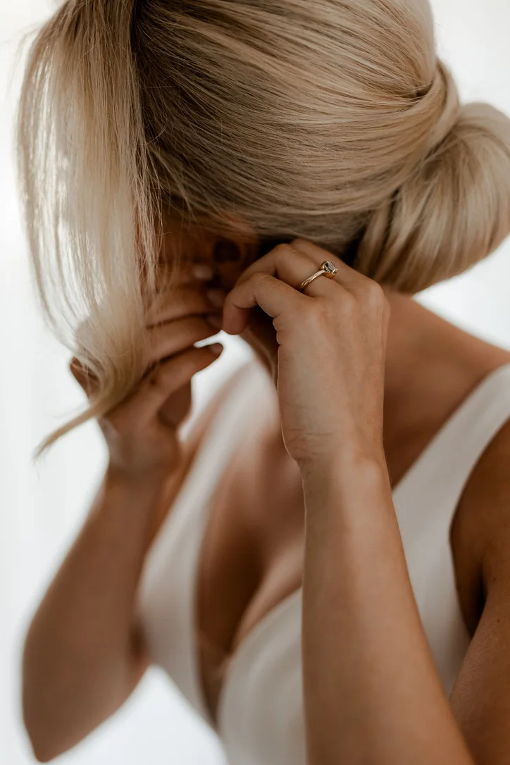 Braut legt beim Getting Ready eine feine Halskette an; ihre blonde Hochzeitsfrisur ist tief gesteckt