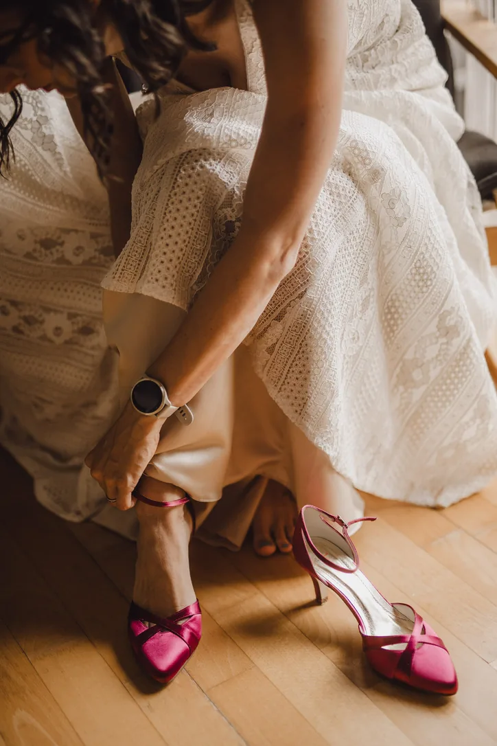 Braut zieht beim Getting Ready leuchtend pinke Brautschuhe zu ihrem Spitzenkleid an