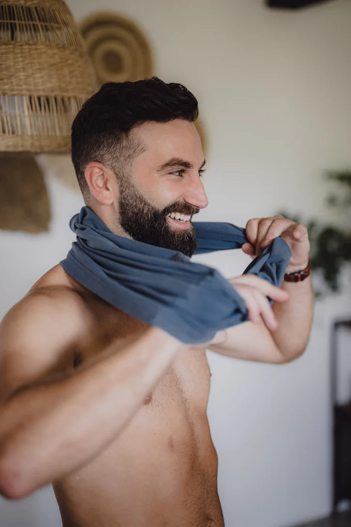 Bräutigam zieht sich beim Getting Ready sein Hemd über und lächelt dabei
