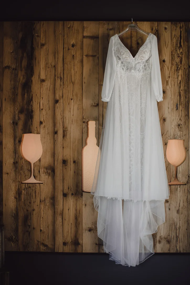 Weißes Brautkleid hängt vor einer rustikalen Holzwand im Zimmer des Hochzeitsweinguts