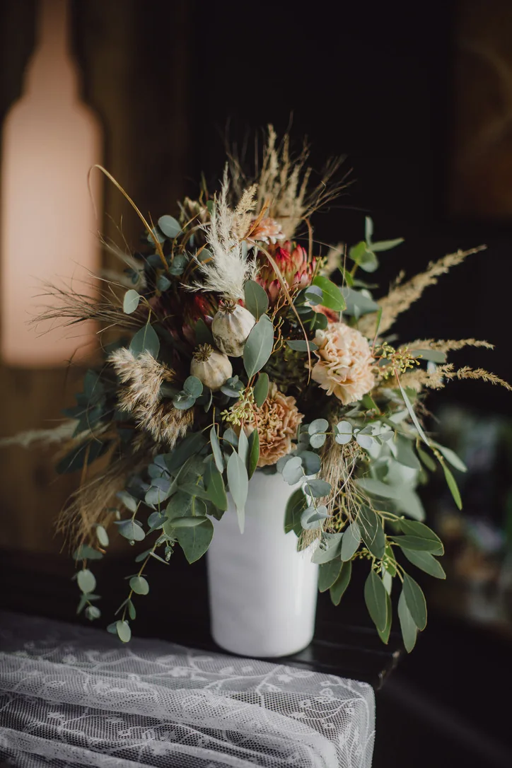 Lockerer Brautstrauß mit Eukalyptus, Gräsern und Blumen in warmen Naturtönen in einer weißen Vase