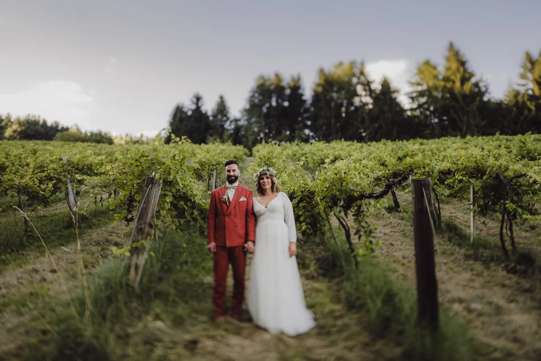 Brautpaar steht gemeinsam zwischen grünen Rebzeilen des Hochzeitsweinguts