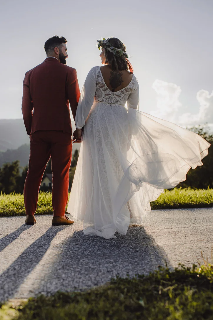 Brautpaar geht Hand in Hand in die Abendsonne, während das Brautkleid im Wind weht