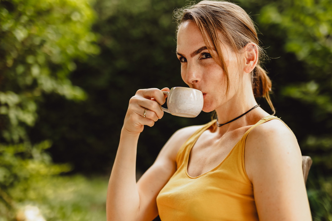 Miriam trinkt aus einer kleinen Kaffeetasse im sonnigen Garten