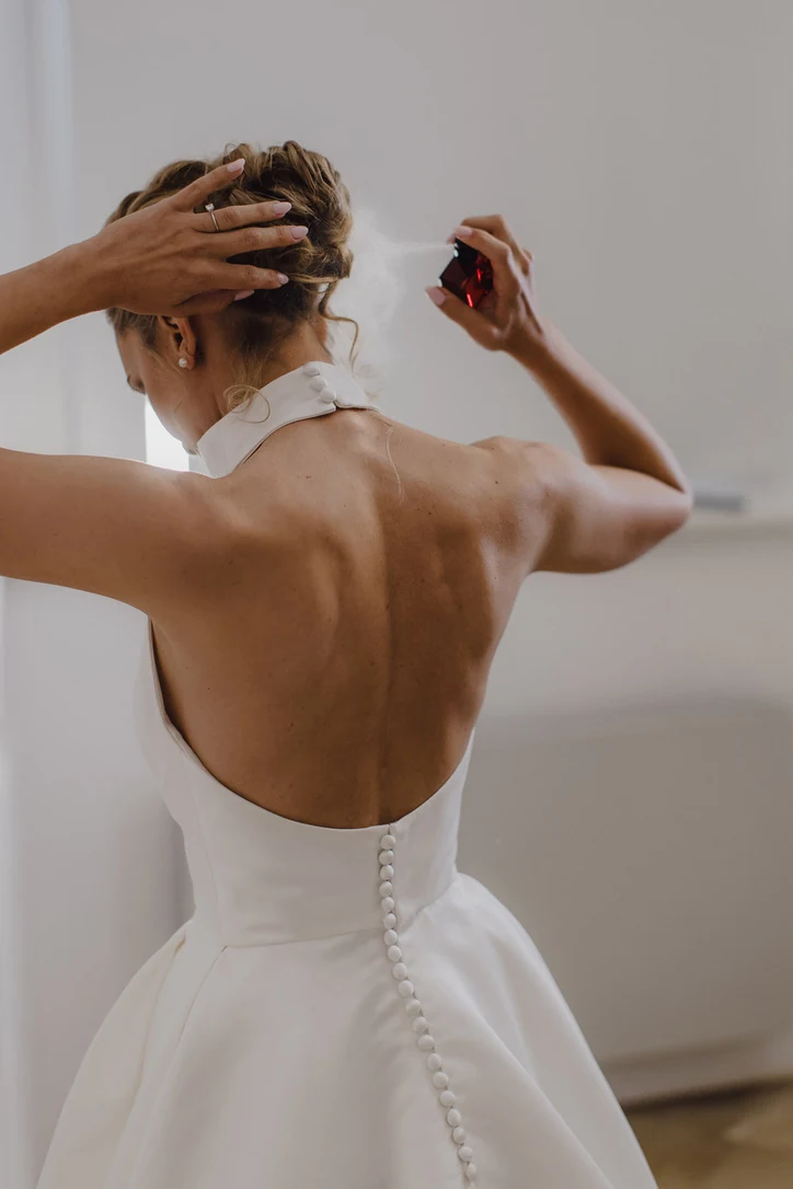 Braut sprüht beim Getting Ready Parfum auf ihren Nacken, aufgenommen von hinten im weißen Kleid